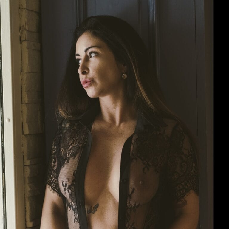 Portrait of a woman with dark hair wearing a black lace robe, looking to the left by a doorway.