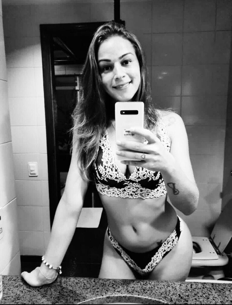 Smiling woman in lace lingerie taking a mirror selfie in a bathroom.